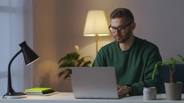 一个晚上在家工作过度的男人，合上笔记本，揉揉眼睛和脸，戴上眼镜视频素材