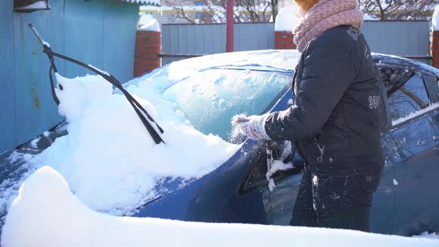 大雪过后，一名妇女正在用车刷清理车上的积雪视频素材