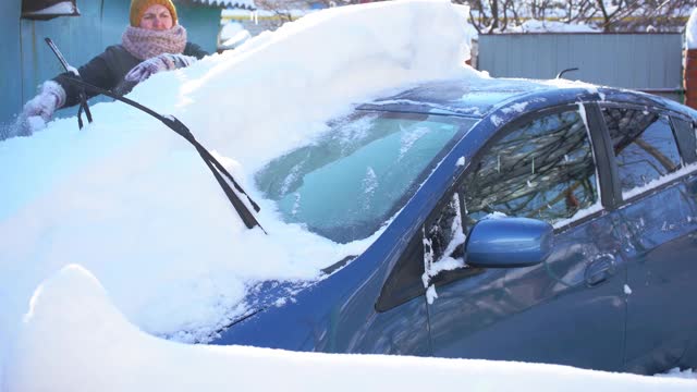 大雪过后，一名妇女正在用车刷清理车上的积雪视频素材