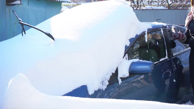 大雪过后，一名妇女正在用车刷清理车上的积雪视频素材