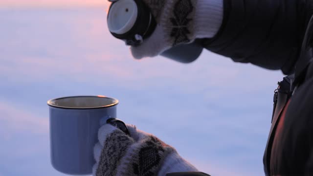 在寒冷的冬天，把热水瓶里的茶倒进杯子里视频素材