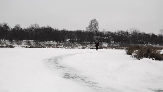 在结冰的湖面上滑冰。穿着白色花样滑冰鞋的女人在结冰的池塘上滑行。穿着休闲装的女性在户外滑冰。冬季运动活动视频素材