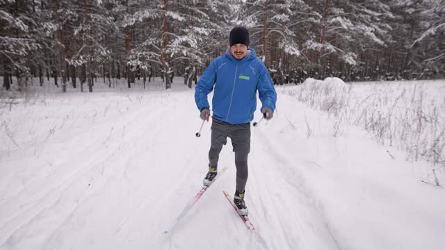 一个年轻人正在冬季森林里进行越野滑雪。运动员滑冰。视频素材