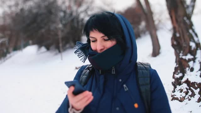 一个年轻女子看手机屏幕上的好消息，寒冷的天气和雪。视频素材