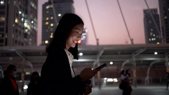 亚洲女商人在城市的夜晚行走和使用智能手机视频素材