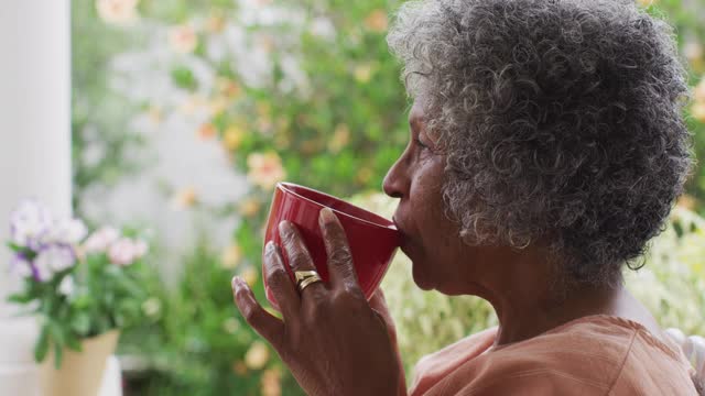 特写的高级非洲裔美国妇女喝咖啡，而坐在门廊的房子视频素材