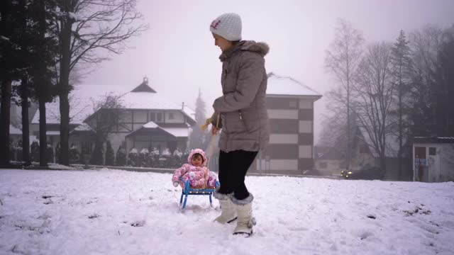 妈妈和小女孩在冬季公园拉雪橇视频素材