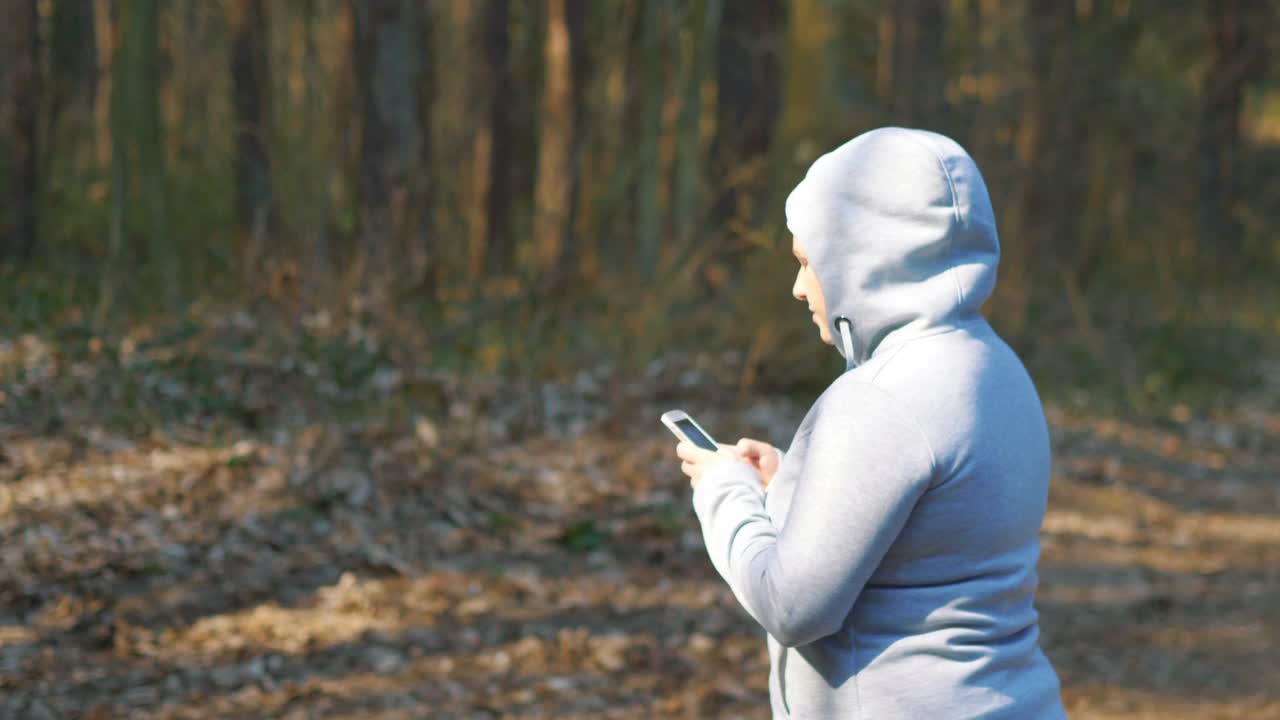 一个女人拿着智能手机在森林里寻找方向，4k慢镜头，每秒60帧视频素材