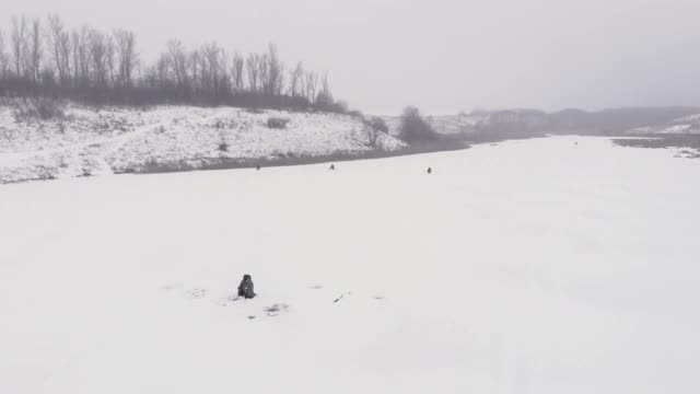 渔夫冬天在结冰的冰湖上钓鱼。一个人拿着钓竿在钓鱼。雄鱼在冰洞附近的冰上捕鱼视频素材