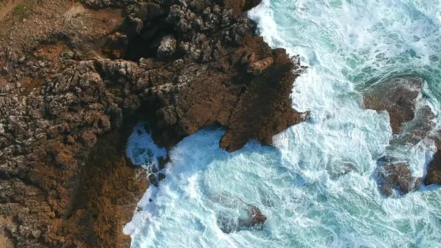 海波与绿松石海水撞击海滩上的岩石鸟瞰图。视频素材