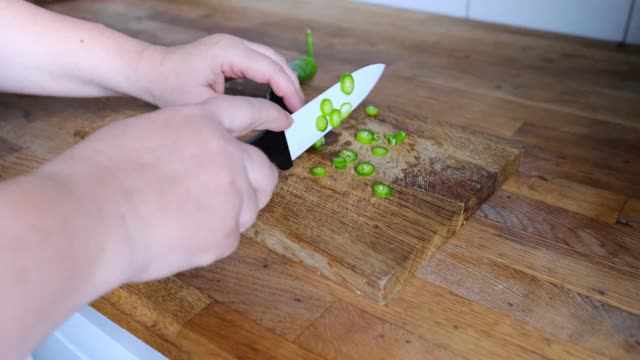 女人手切成红辣椒薄片，将红辣椒放在木桌上，在家做健康食品的概念，提供餐饮服务视频素材