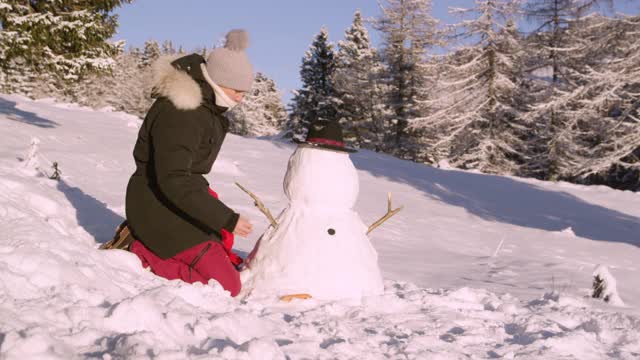 特写:一个快乐的年轻女子正在一个阳光明媚的冬日里堆雪人。视频素材