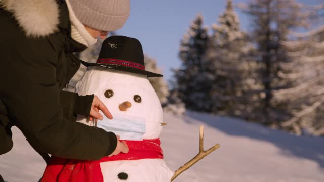 特写:年轻的白人妇女给滑稽的雪人戴上了外科口罩。视频素材