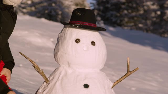 近景:好玩的女人把胡萝卜鼻子和红围巾放在滑稽的雪人上。视频素材