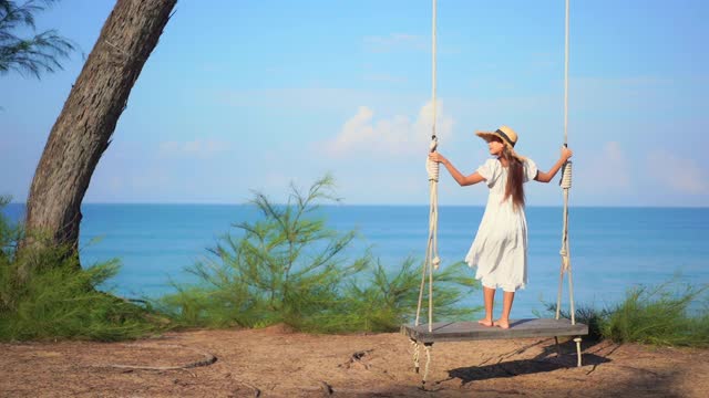 亚洲女人坐在吊床上绕着海、滩、海摇摆视频素材