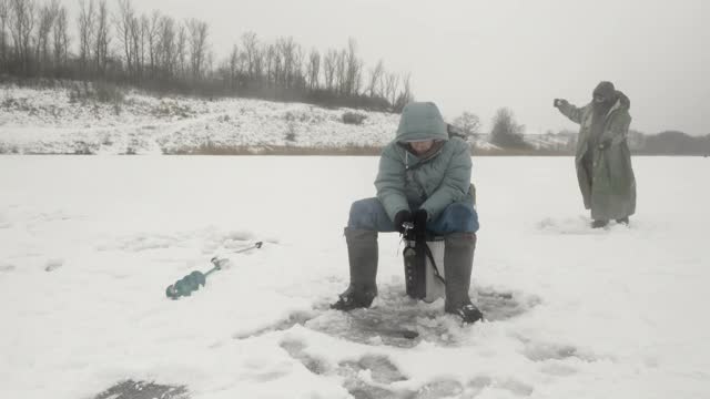 渔民们冬天在结冰的河里钓鱼。穿着冬季极端服装的男人在冰洞里捉鱼视频素材