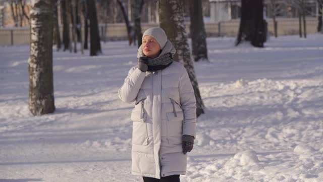 在寒冷的日子里，孕妇穿着暖和的夹克，带着兜帽，走在下雪的公园里视频素材