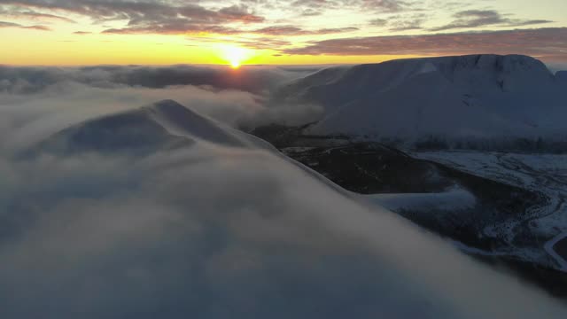 在夕阳中飞过白雪皑皑的山峰。鸟瞰图。山上五颜六色的冬季日落。视频下载