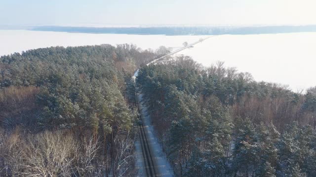 航拍白色越野车行驶在积雪覆盖的森林道路上。在冬天，汽车在结冰的森林路线上行驶。自动驾驶越过美丽的自然之路。旅行和周末活动的概念。以上观点视频素材