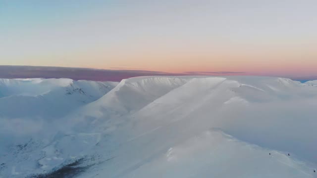 在日落时飞过白雪皑皑的山脉。鸟瞰图。山上五颜六色的冬季日落。视频素材