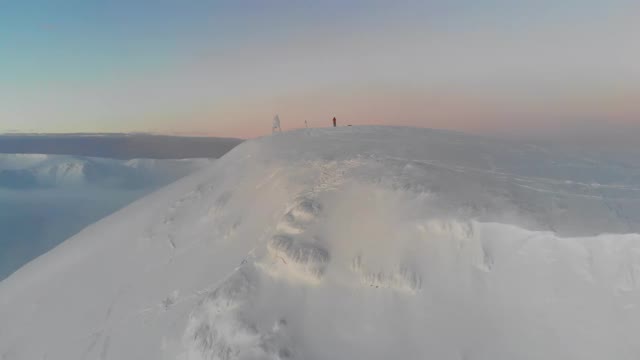 一个男人站在一座白雪皑皑的山顶上。从无人机上看。鸟瞰图。视频下载