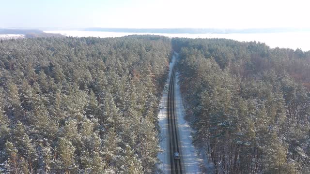 航拍白色越野车行驶在积雪覆盖的森林道路上。在冬天，汽车在结冰的森林路线上行驶。自动驾驶越过美丽的自然之路。旅行和周末活动的概念。以上观点视频素材