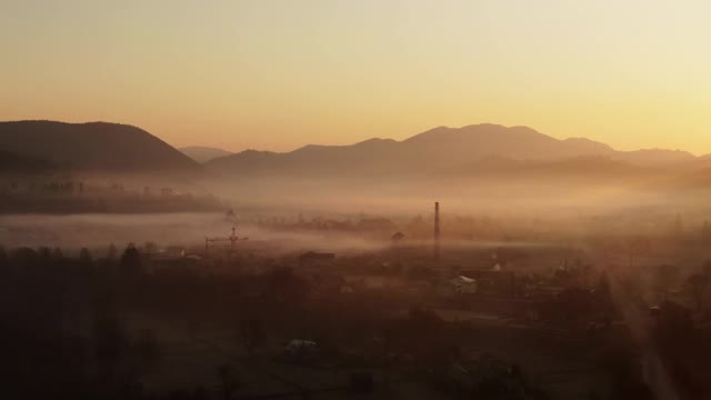 在雾霾的早晨，拍摄高原地区宁静的聚落风景。日出，山村在雾和一切美好在黄色的光-鸟瞰图视频素材