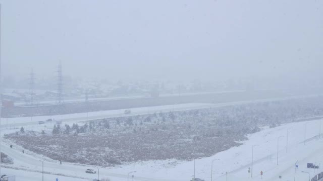 城市里下起了暴风雪，大片雪花从空中飘落下来。由于能见度低，道路上交通拥挤视频素材