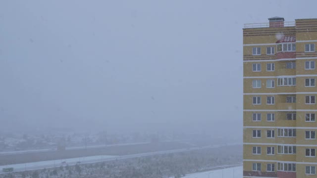 大片的雪花从天空飘落到城市。多层建筑和移动的汽车道路的观点视频素材