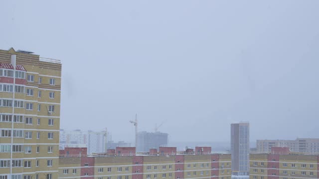 大片雪花从城市的天空中飘落，俯瞰着多层建筑的屋顶和建筑起重机视频素材