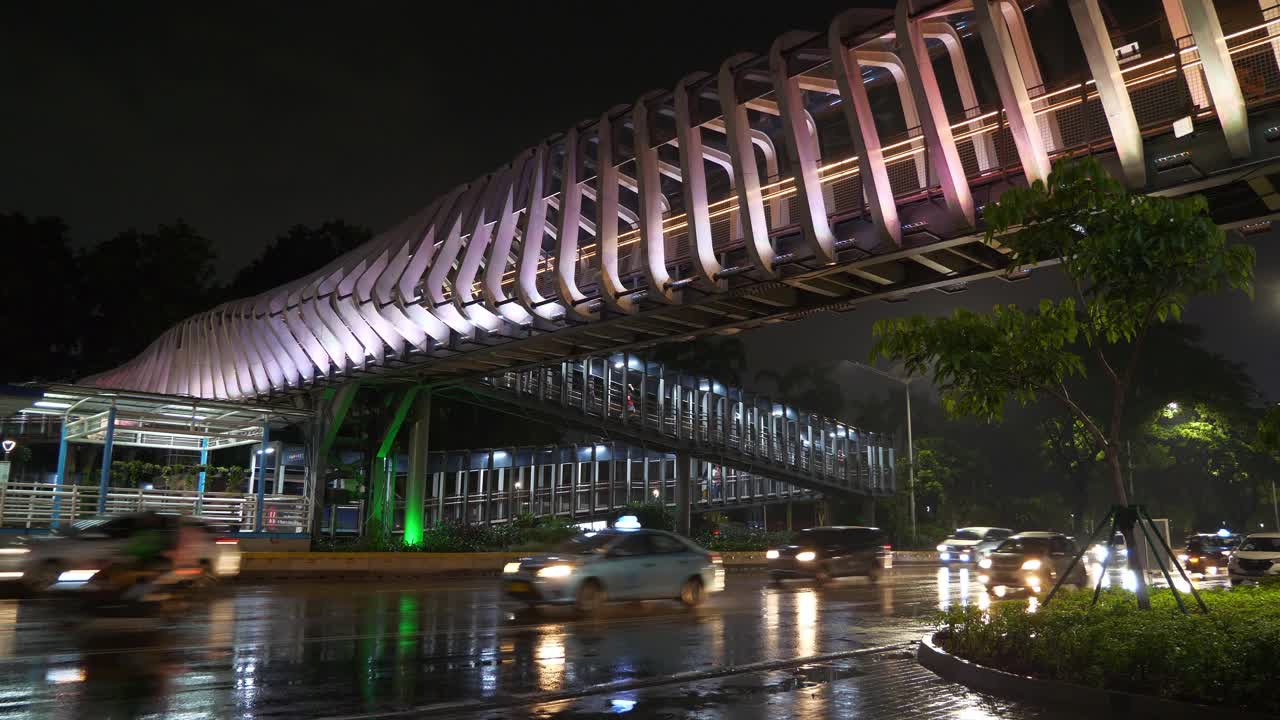 雨夜雅加达市区灯火通明的交通大街，著名的现代步行桥全景4k印尼视频素材