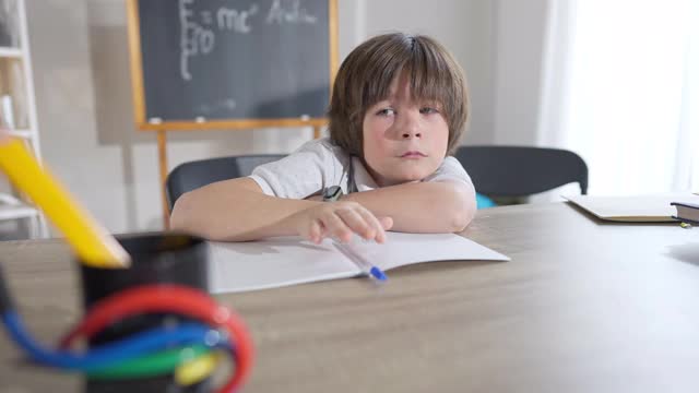 一个黑发白人学生在教室书桌前哭。一幅沮丧不堪的男孩坐在学校室内的肖像。教育问题与悲伤观念。视频素材