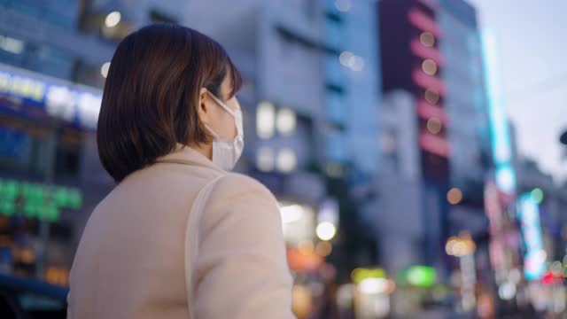 晚上在城市街道上行走的妇女用保护性面罩遮住脸视频素材