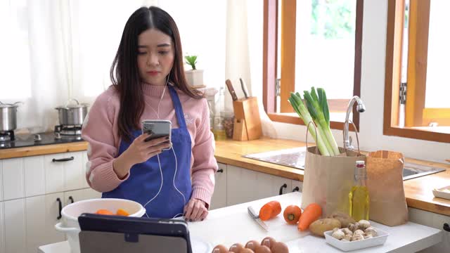 年轻的亚洲女人在厨房里听音乐视频素材