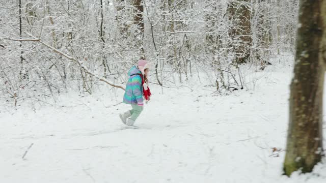 可爱的小女孩穿着五颜六色的衣服在雪地里奔跑。冰雪森林里的冬姑娘。漫步冬日森林视频素材