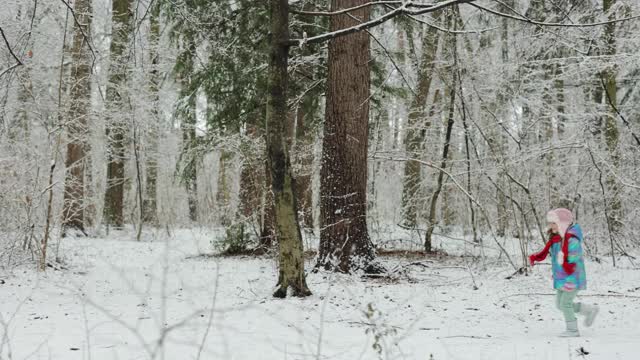 小女孩穿着五颜六色的衣服在雪地里奔跑。冰雪森林里的冬姑娘。在冬天的森林里漫步。表达积极的情绪，真正明亮的情绪，微笑视频素材