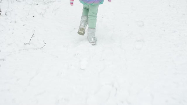 可爱的小女孩穿着五颜六色的衣服和帽子在雪地里奔跑。冰雪森林里的冬姑娘。走在森林里视频素材