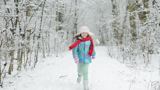 一个快乐的小女孩穿着冬天的衣服在下雪的冬天里跑步。快乐的小女孩在冬天玩雪。女孩喜欢冬天，有霜冻的日子视频素材