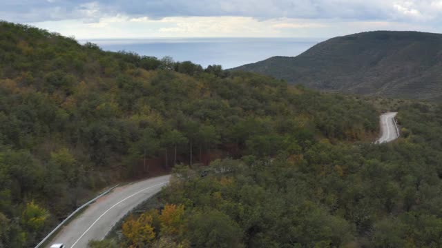 空中景观越野车行驶在蜿蜒的道路之间的绿色牧场和山脉。越野车在阴天的青山高地上蜿蜒行驶视频素材