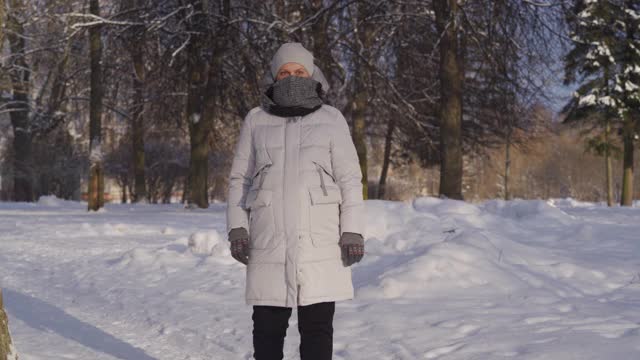 在寒冷的日子里，孕妇穿着暖和的夹克，带着兜帽，走在下雪的公园里视频素材