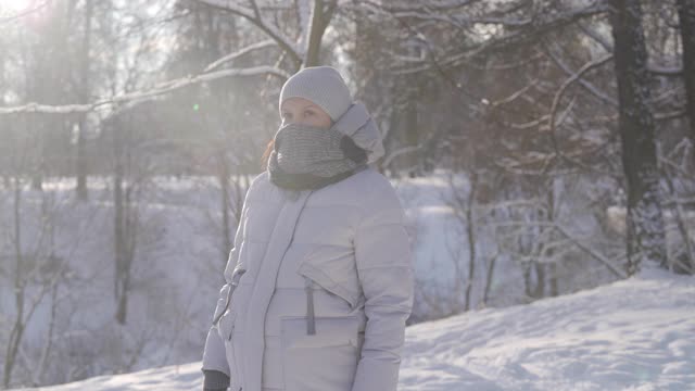 在寒冷的日子里，孕妇穿着暖和的夹克，带着兜帽，走在下雪的公园里视频素材