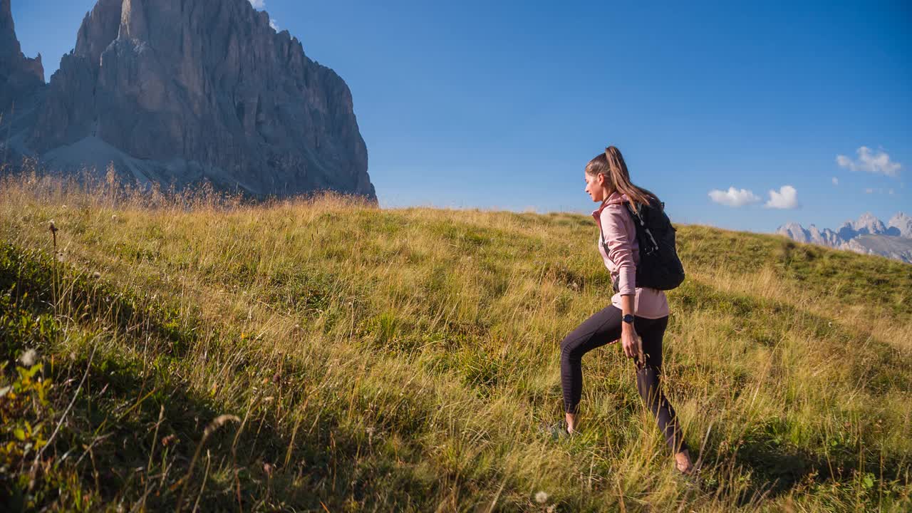 女人是活跃的，在雄伟的山前的草地上徒步旅行视频素材