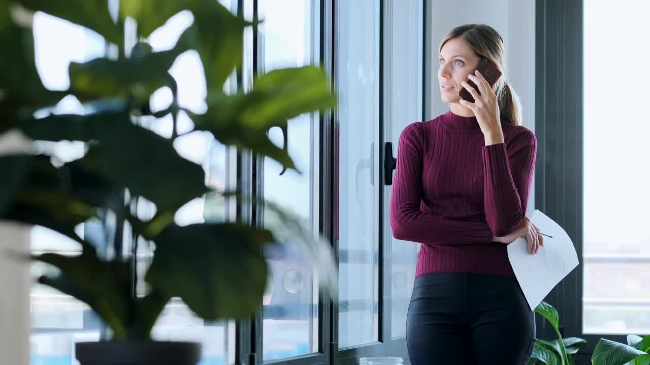 在办公室里用智能手机看窗外的女商人视频素材