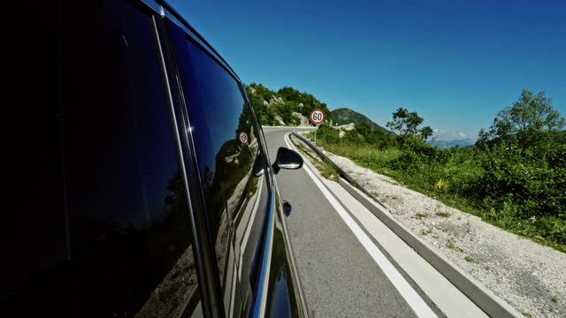 在一个阳光明媚的日子里，一辆在山区高速公路上行驶的汽车沿着碰撞护栏通过交通速度标志，宽镜头视频素材