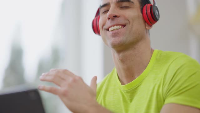 一个面带微笑的中东男子戴着耳机在室内随着音乐跳舞的特写。帅气自信的年轻人在家里享受业余爱好的大头照。生活方式和快乐理念。视频素材