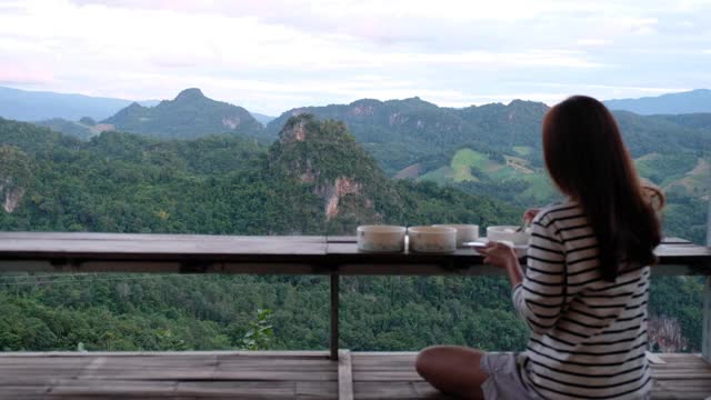 后视图的一个女人准备食物吃，而坐在阳台上与绿色植物山景视频素材