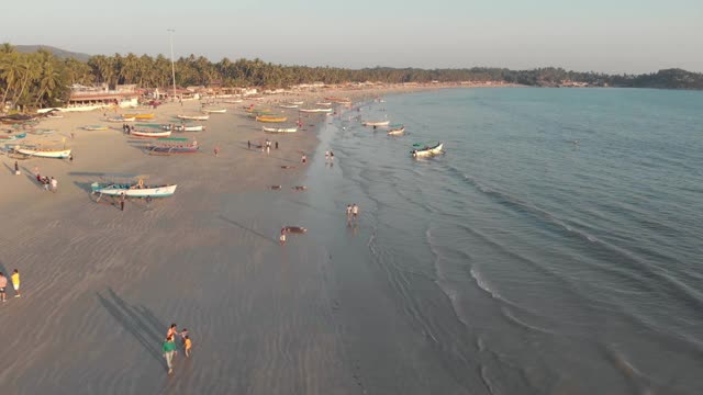 游客们在Palolem海滩，沿着海岸附近的金色沙滩漫步，渔船停泊在那里视频素材