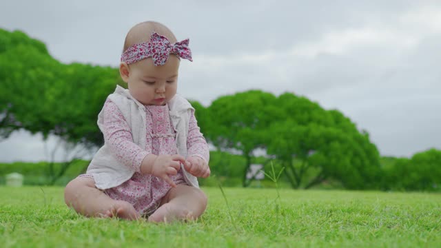 有趣的小白人婴儿坐在公园的绿色草坪上。学习和研究周围的世界。视频素材