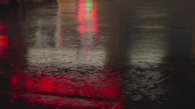 雨点在夜晚城市明亮的灯光背景下从汽车玻璃上流下。雨夜。汽车通过十字路口。鲜艳的交通灯。视频素材