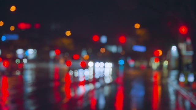 雨点在夜晚城市明亮的灯光背景下从汽车玻璃上流下。雨夜。汽车通过十字路口。鲜艳的交通灯。视频素材